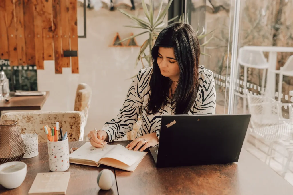 Photo de Audrey Leger, concentrée en train de dessiner sur son carnet , avec son ordinateur posée devant elle.