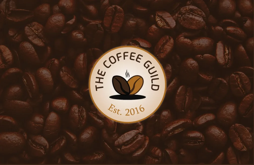 Logo "The Coffee Guild" représentant deux grains de cafés marron et beige avec de la fumée s'échappant par le dessus. Le fond de l'image est des grains de café.