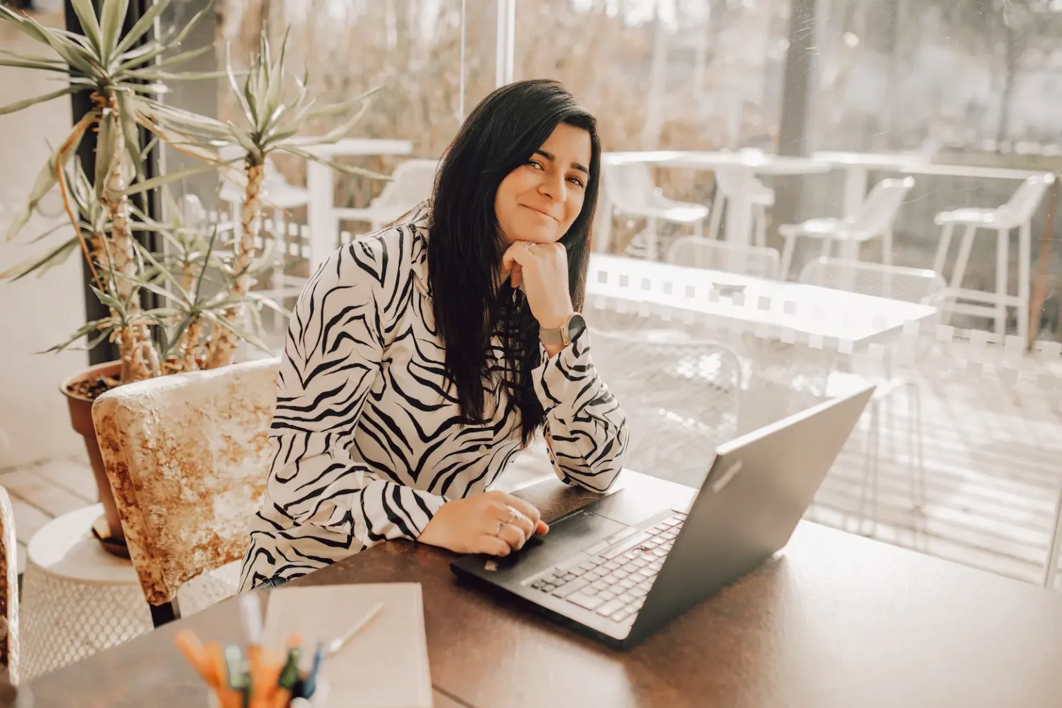 Photo représentant un portrait de Audrey Leger, qui regarde l'objectif en souriant avec son ordinateur ouvert sur une table devant elle.