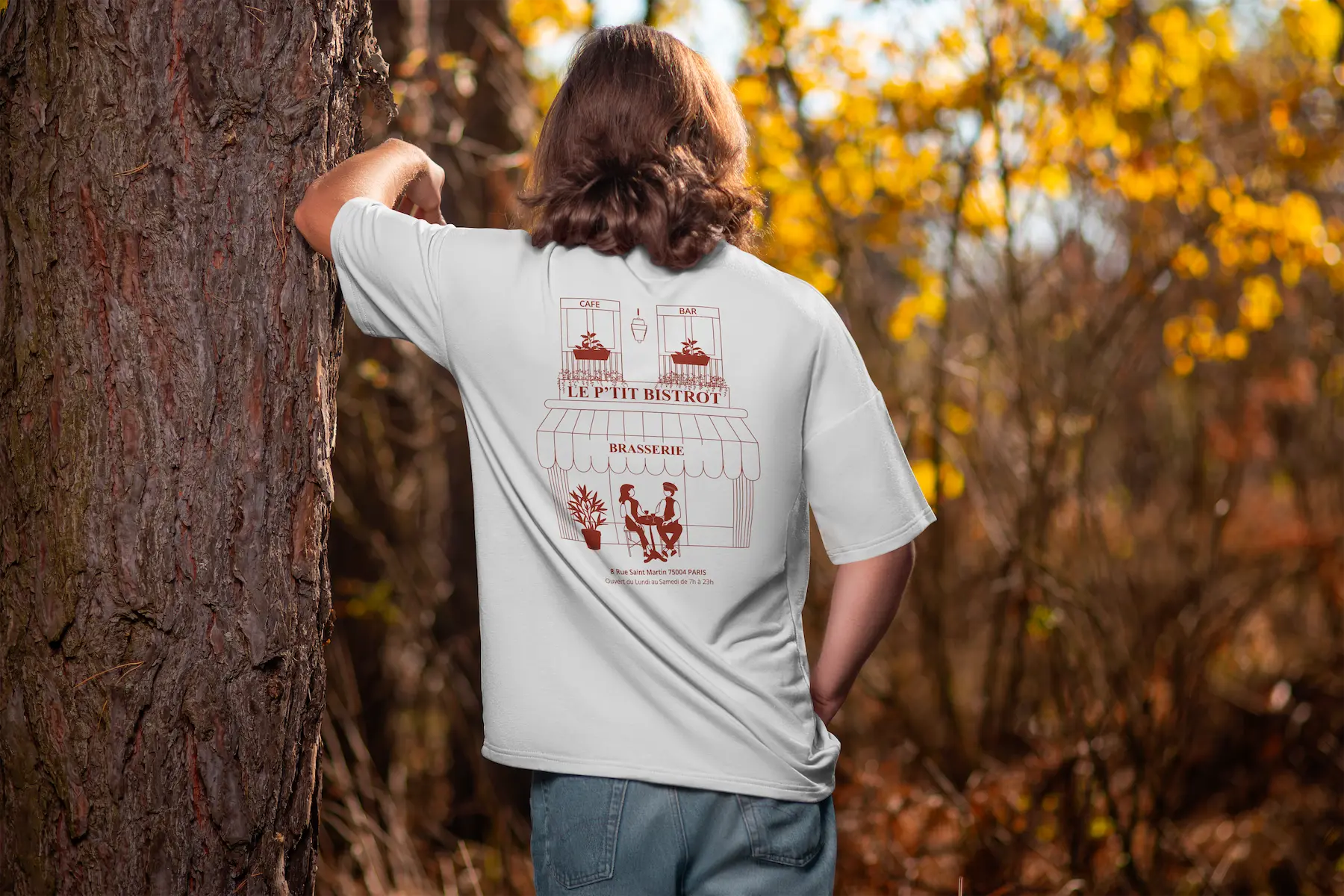 Homme de dos dans la nature , accoudé à un arbre, portant un Tshirt Blanc, avec en illustration la devanture d'une brasserie parisienne : " le p'tit bistrot"